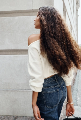 Model is wearing a white off shoulder sweater and dark wash jeans.