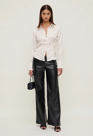 Model is wearing a white satin shirt and black faux leather pants.