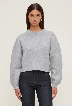 Model is wearing a grey sweater and dark wash jeans.